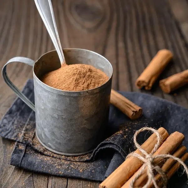 ground cinnamon in a metal cup with cinnamon sticks beside it for health benefits of cinnamon and what is true cinnamon