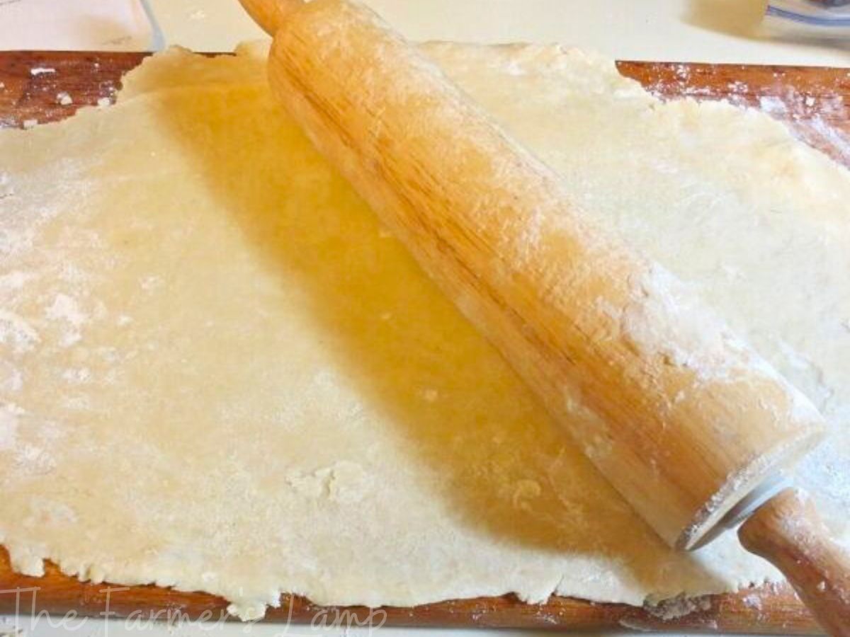 einkorn flour pie crust rolled out on a wooden pastry board with a rolling pin on it