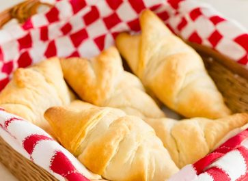 homemade einkorn crescent rolls in a basket lined with red and white checkered fabric
