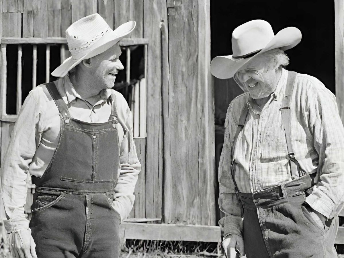 black and white photo of two old farmers laughing while standing in front of a barn as they talk about old sayings and their meanings