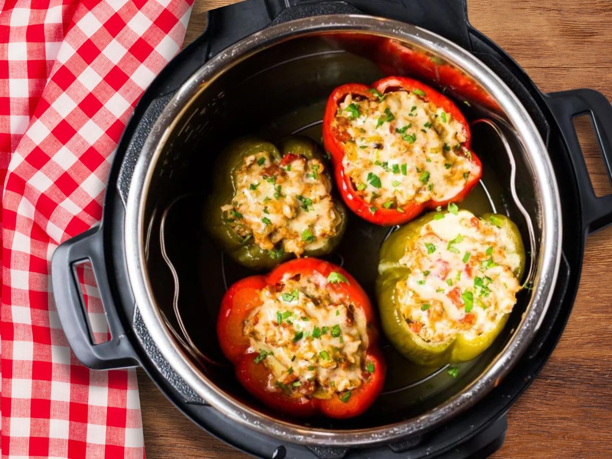 two red and two green stuffed peppers in an instant pot sitting on a wooden surface with a red gingham tablecloth beside it